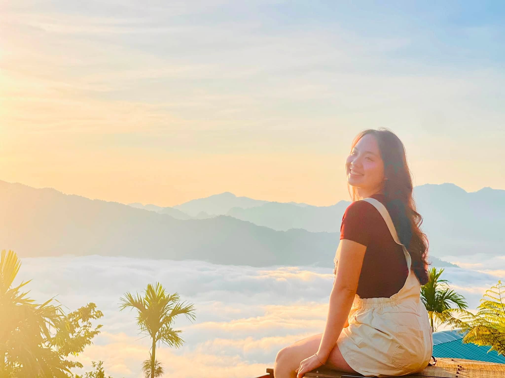 Cô gái ngồi quay nghiêng, mỉm cười đón nắng sớm trên biển mây
