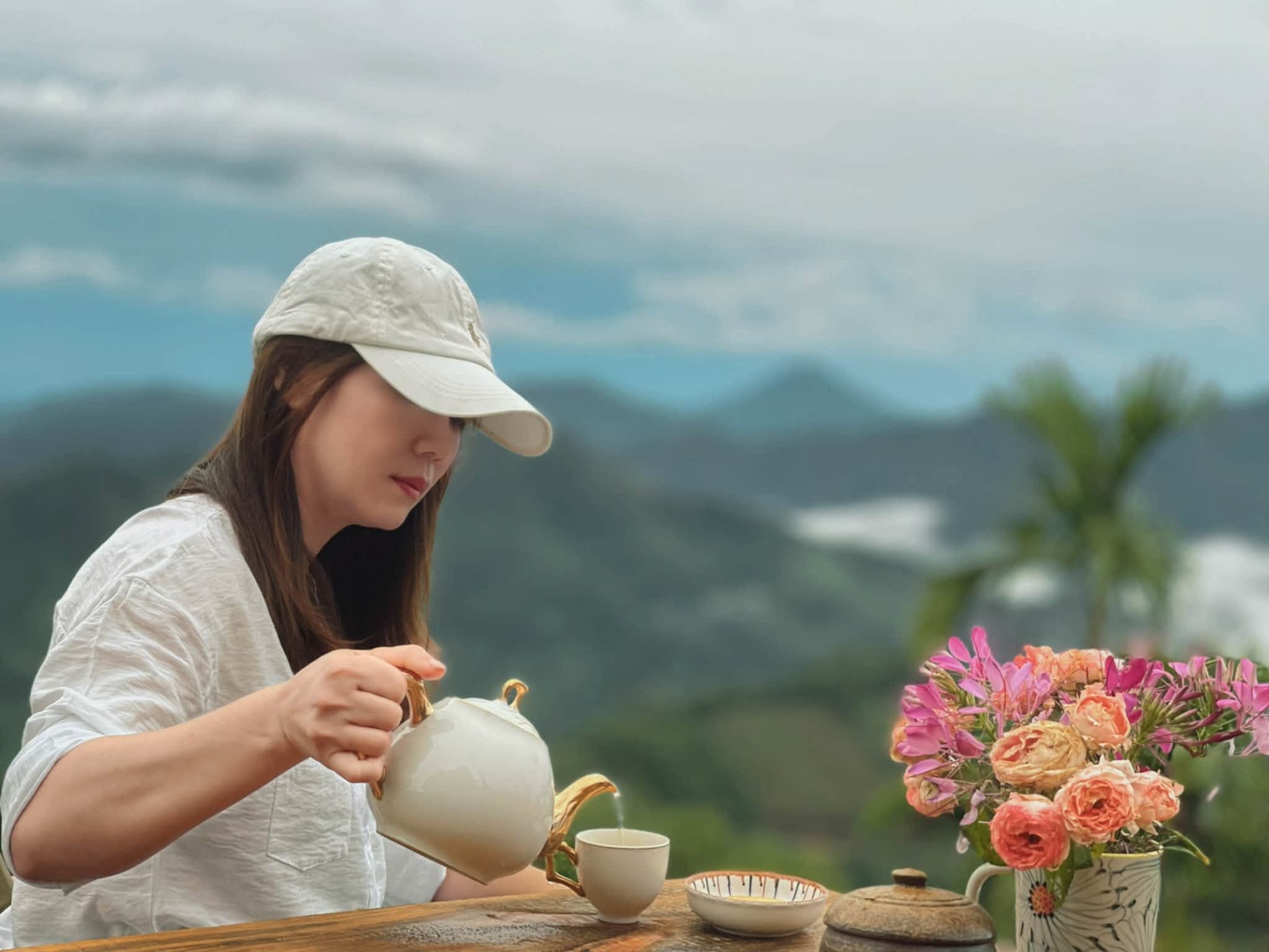 Khách nữ đội mũ trắng rót trà bên khung cảnh núi rừng mờ sương