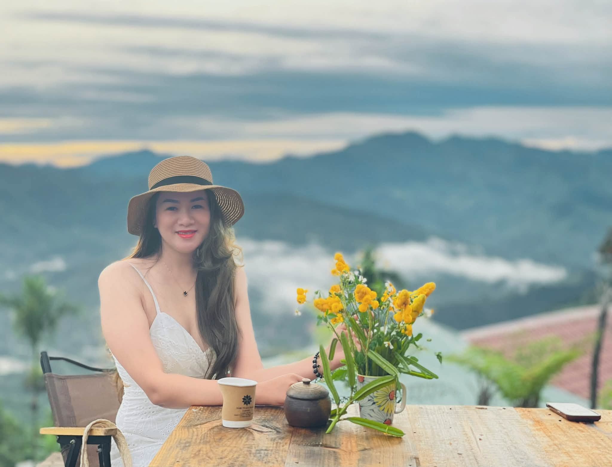 Nữ du khách đội mũ cói ngồi bên tách cà phê ngắm mây núi