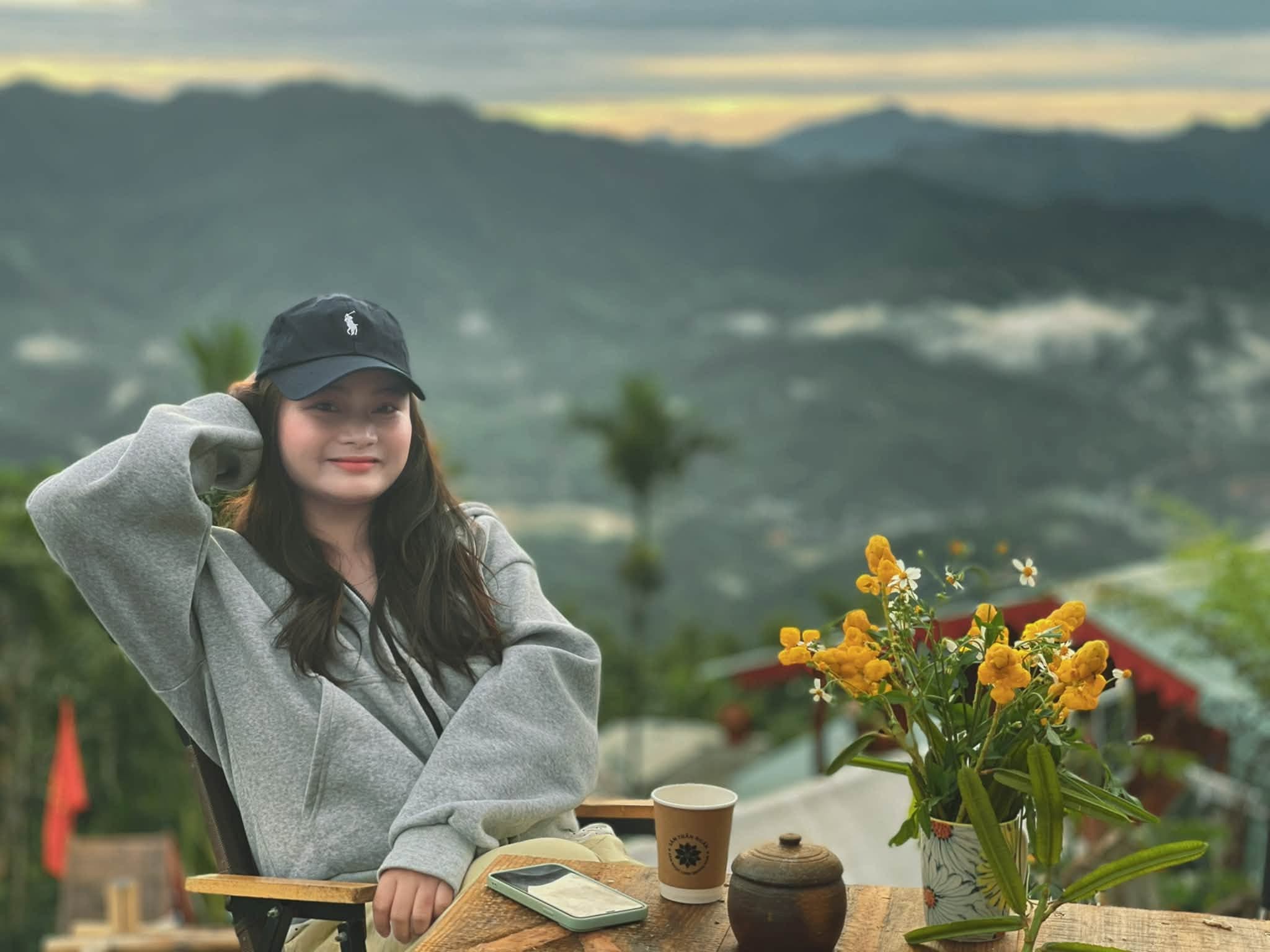 Du khách áo hoodie xám thư giãn bên bàn trà ngắm hoàng hôn núi
