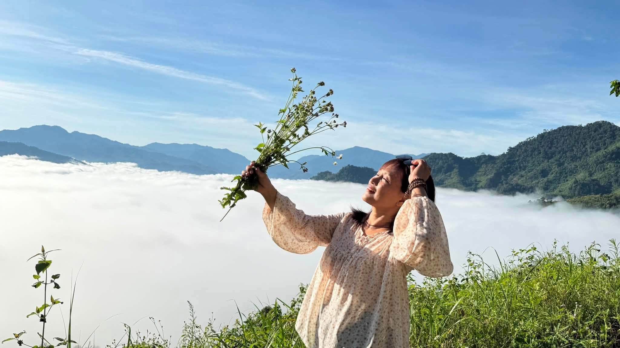 Du khách cầm bó hoa dại ngước nhìn trời giữa biển mây bồng bềnh