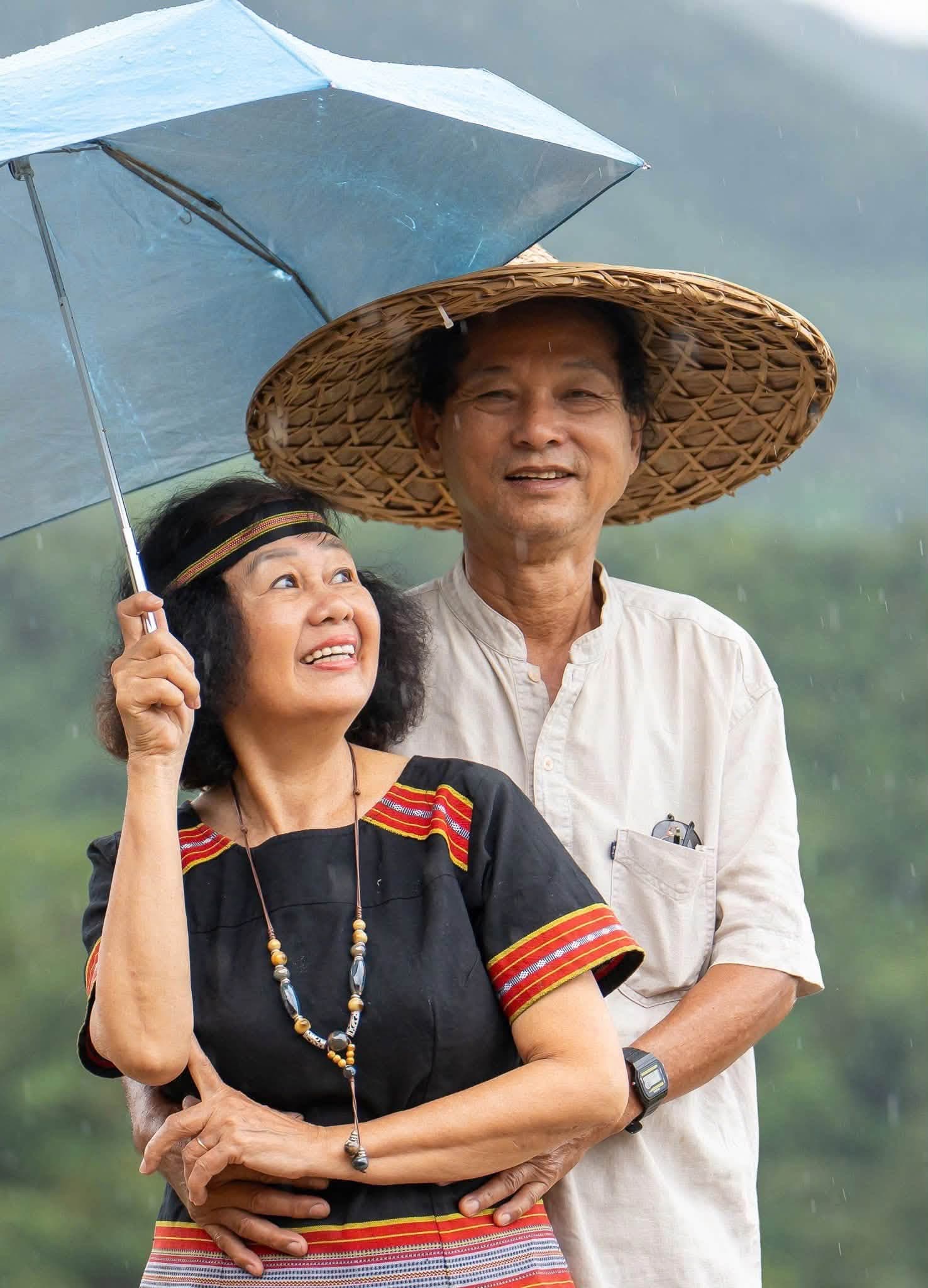 Đôi vợ chồng lớn tuổi trang phục dân tộc che ô dưới mưa núi