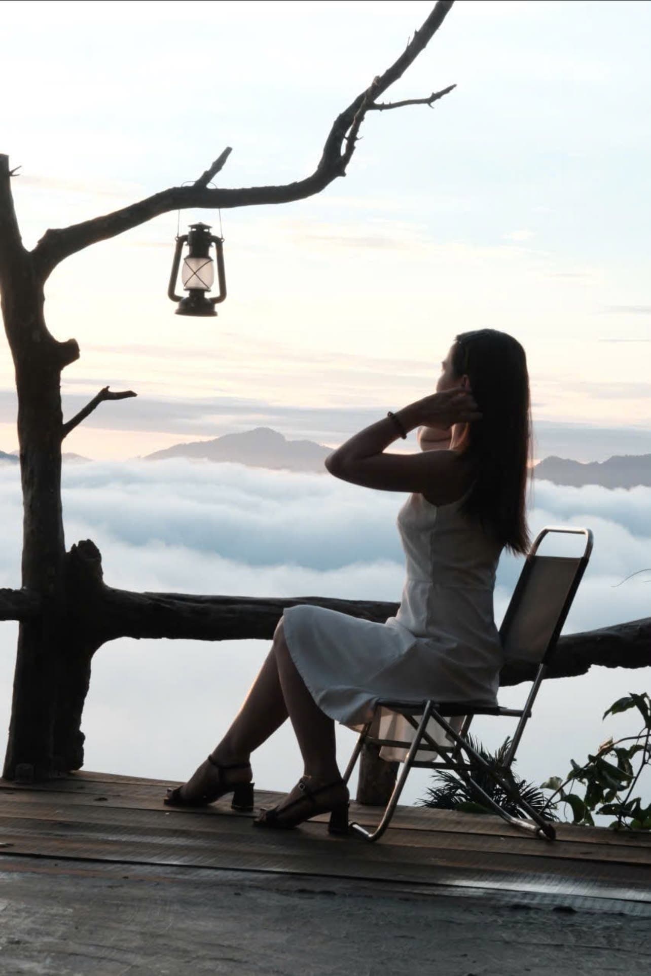 Cô gái váy trắng ngồi ngắm biển mây bên cây khô treo đèn lồng