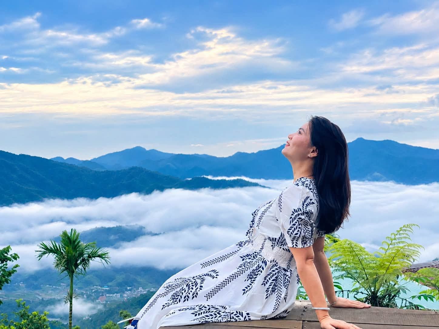 Cô gái áo hoa xanh ngồi ngắm mây trời, tóc bay trong gió núi