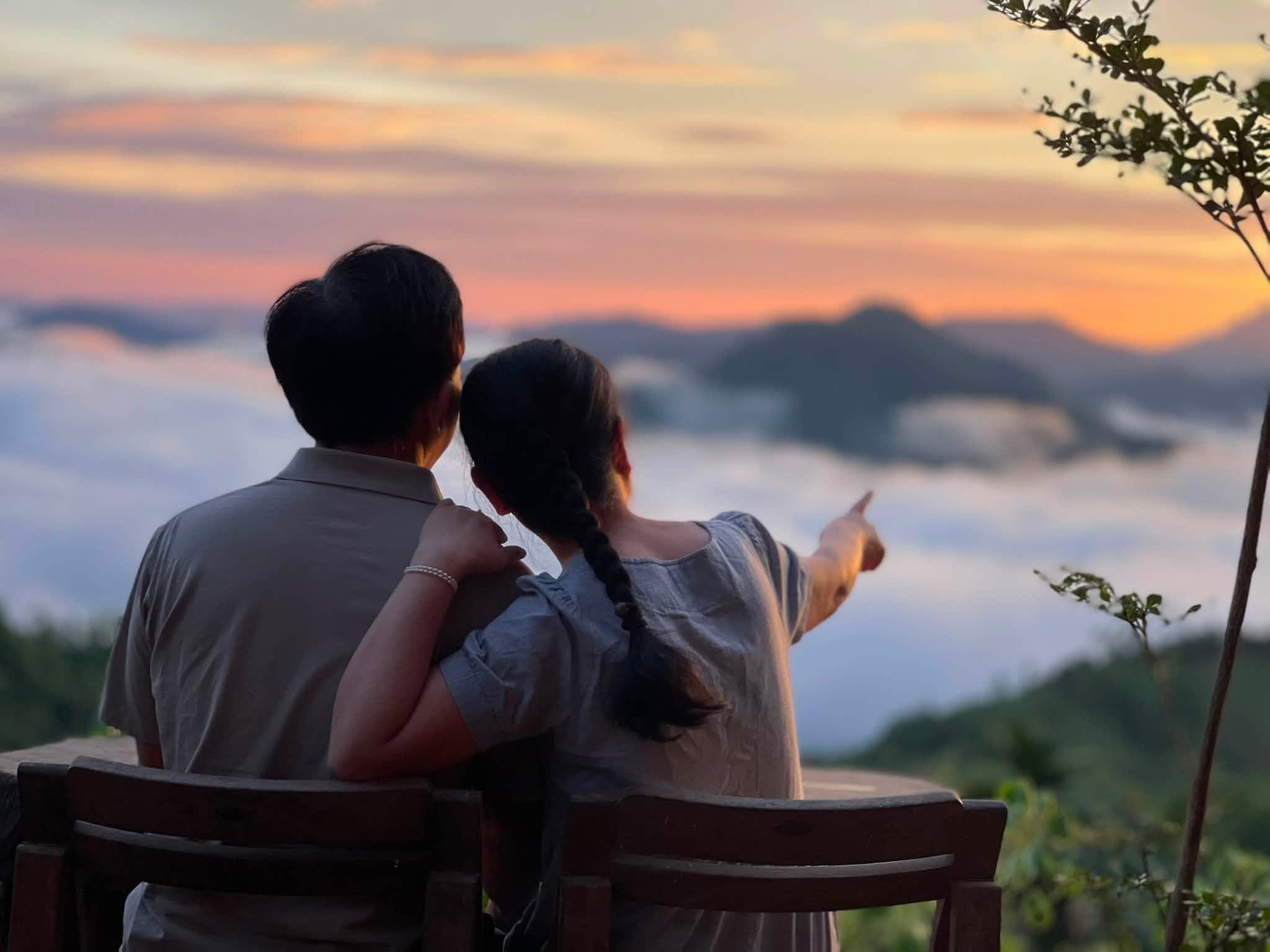 Đôi bạn trẻ ngồi bên nhau, chỉ tay về phía biển mây hoàng hôn