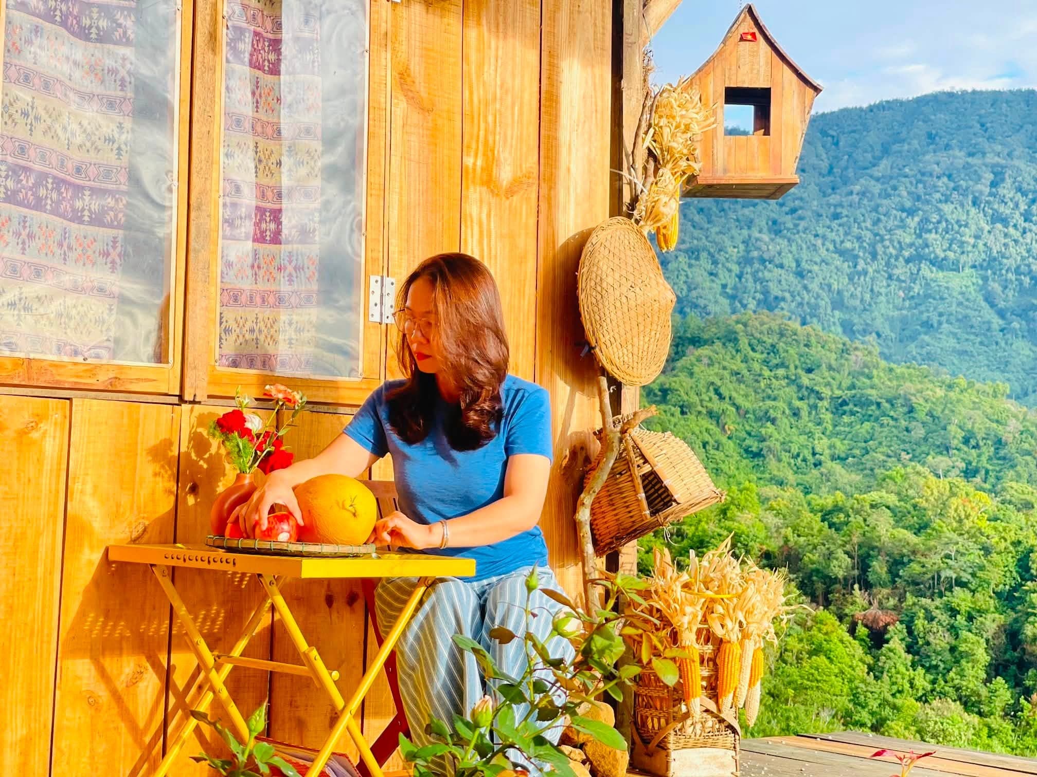 Khách nữ thư giãn bên hiên nhà gỗ, nắng chiều rừng núi